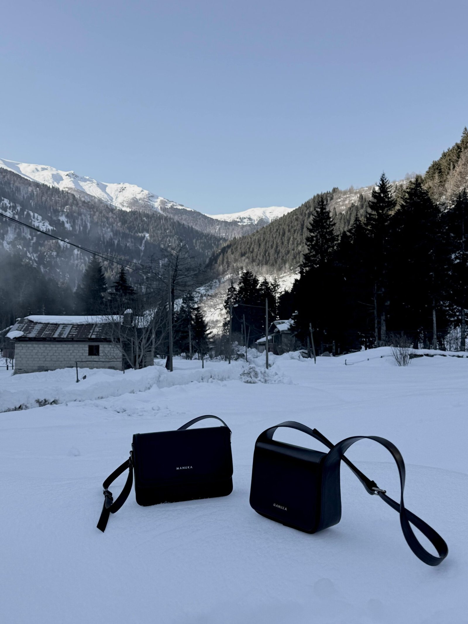Two stylish shoulder bags set against a serene snowy mountain backdrop, ideal for winter fashion.